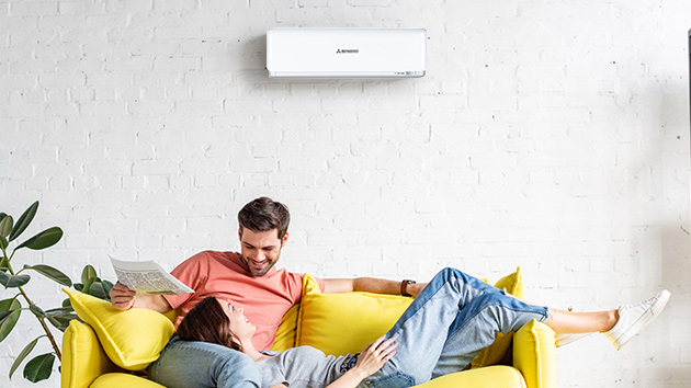 couple sitting on lounge underneath mitsubishi heavy industries split system air conditioner