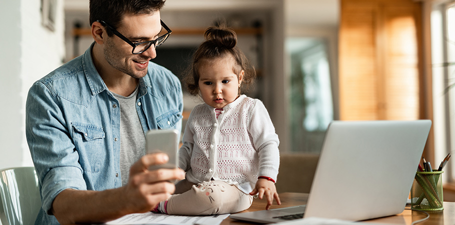 dad working from home inside with his daughter on table showing her phone